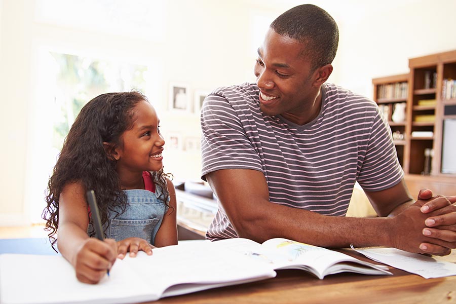 Personal Insurance - Father and Young Daughter Smile at Each Other as He Helps Her With Her Homework at the Kitchen Table